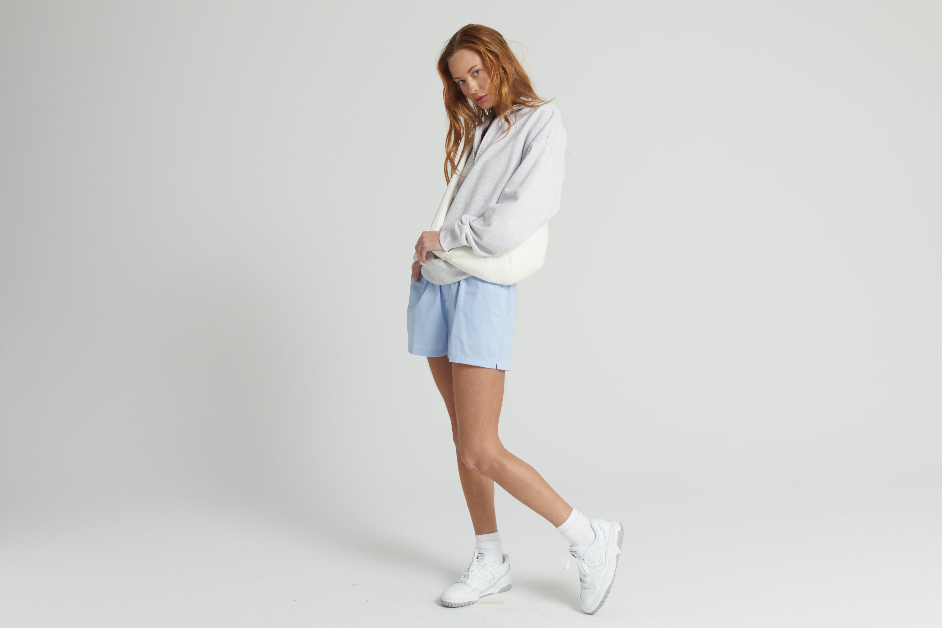 Woman wearing a light gray sweatshirt and blue shorts on a white background