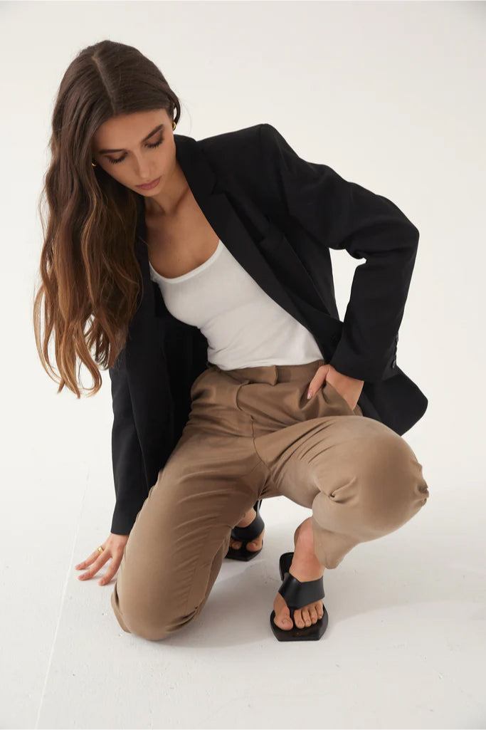 Woman in black blazer and beige pants posing on a white background
