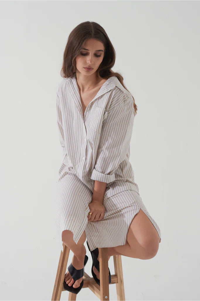 Woman wearing a striped dress sitting on a stool against a white background