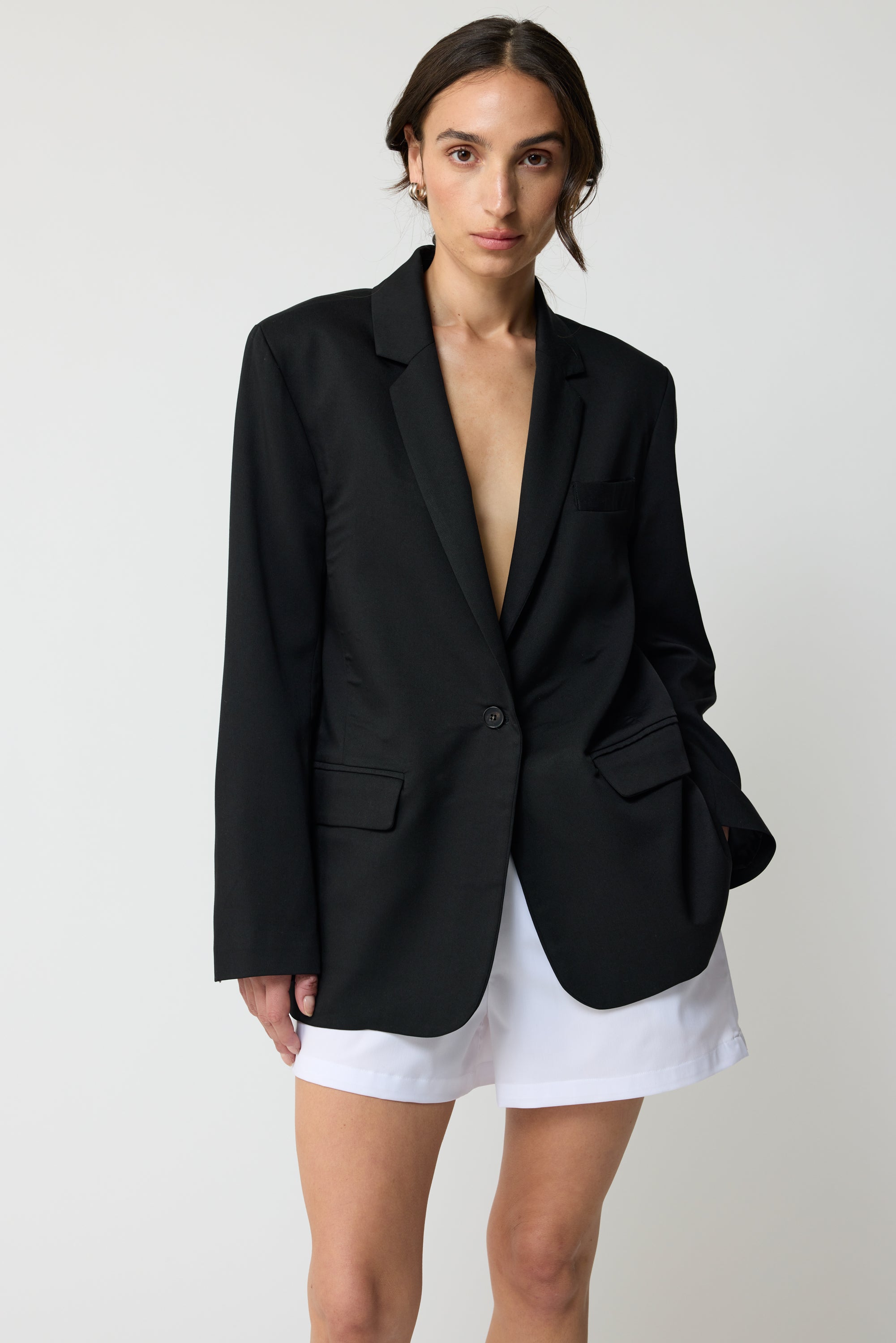 Woman wearing a black blazer over white shorts with a plain background