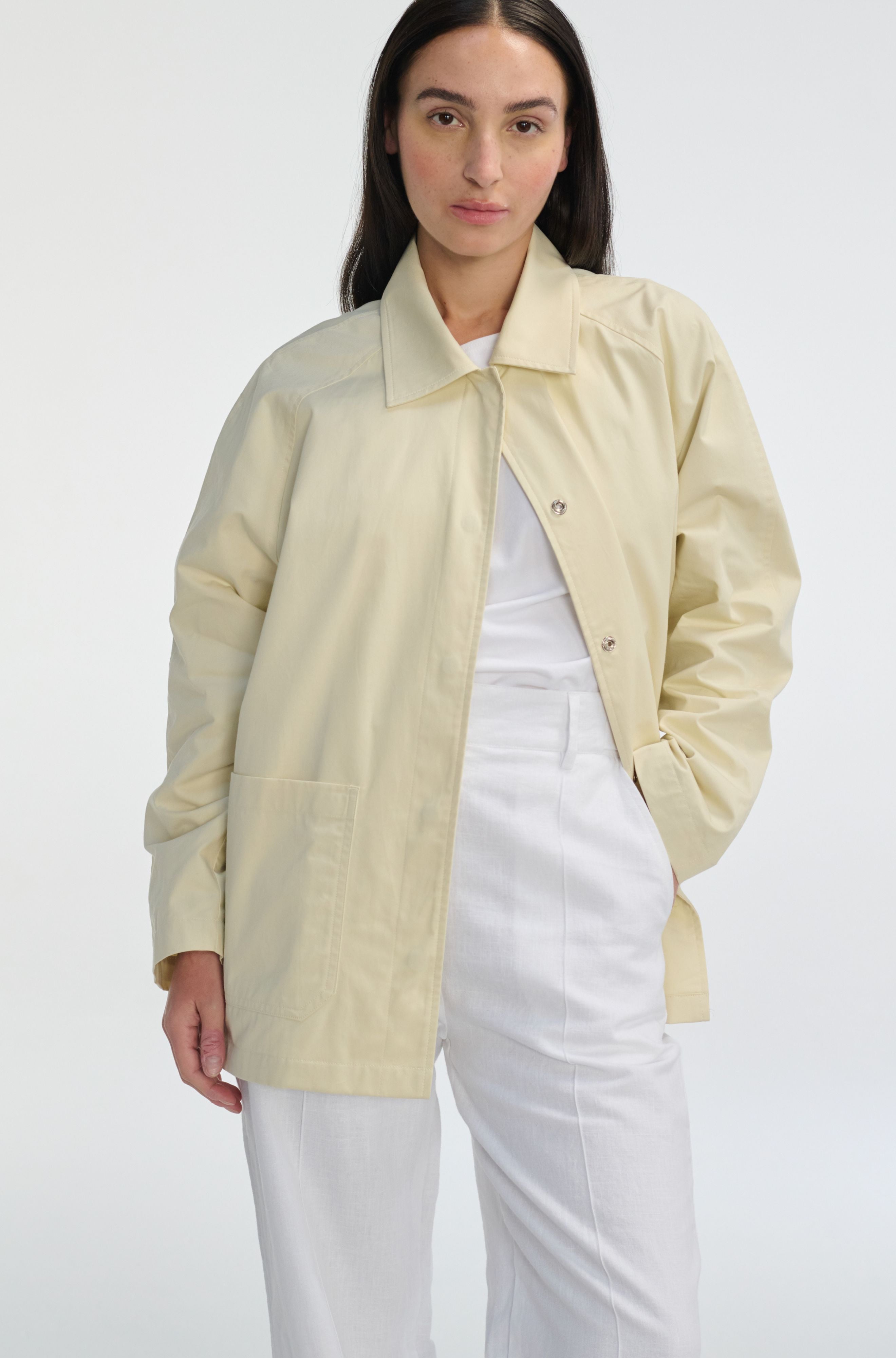 Woman wearing a light beige jacket over a white top and pants on a white background