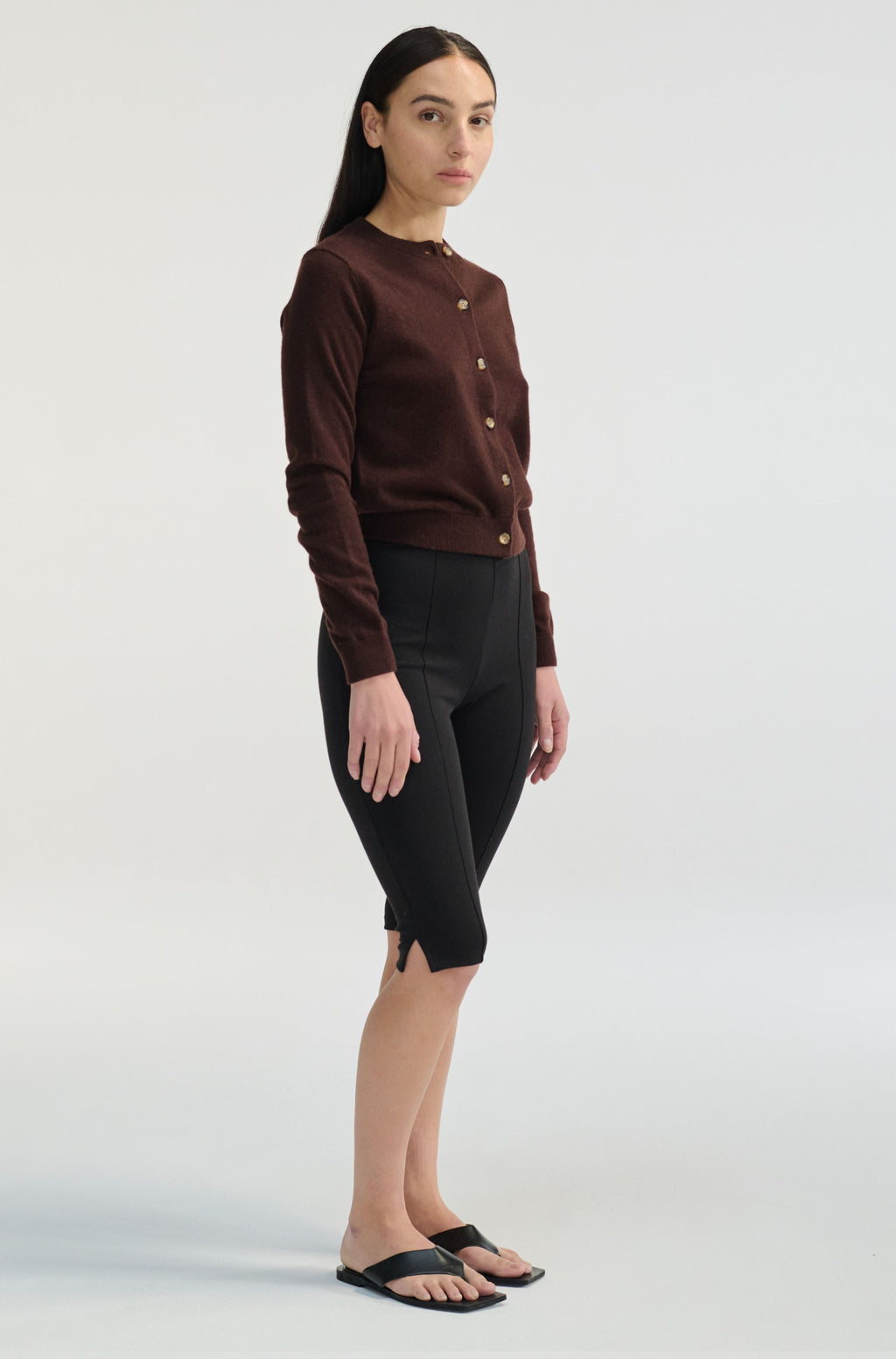 Woman wearing a brown button-up shirt and black pants on a white background