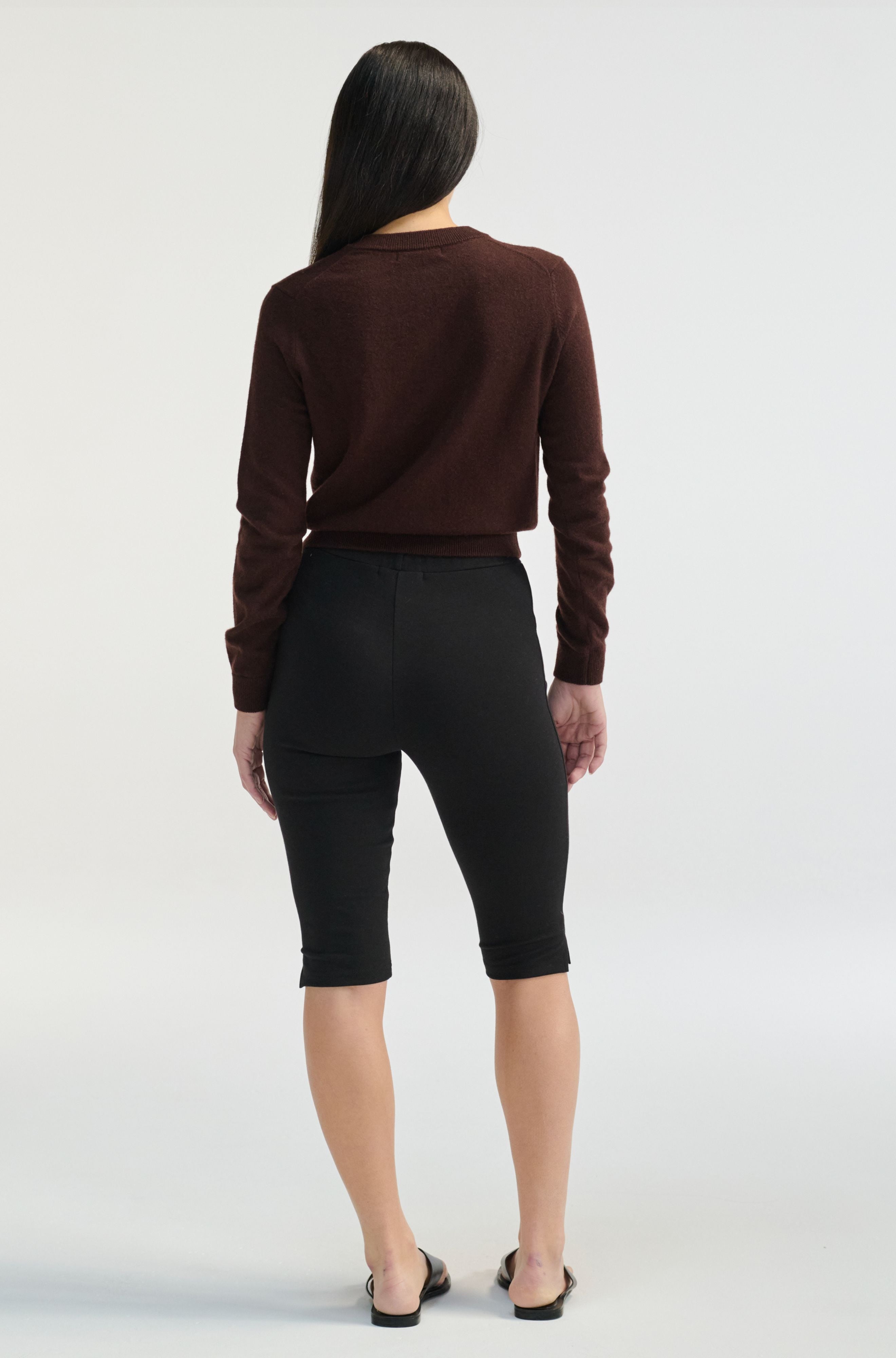Person wearing a brown sweater and black pants on a white background