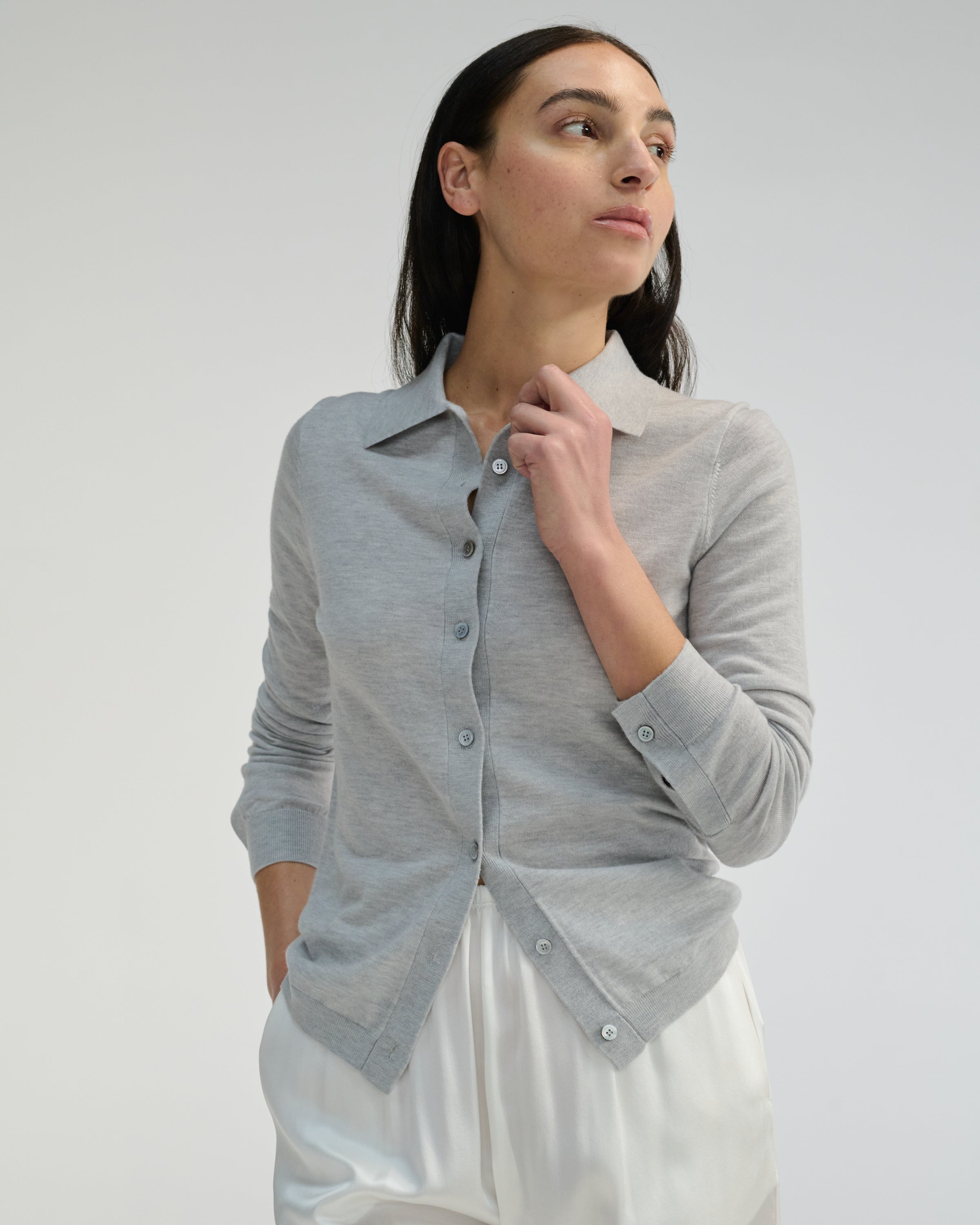 Woman wearing a gray button-up shirt over a white silk pants on a plain background