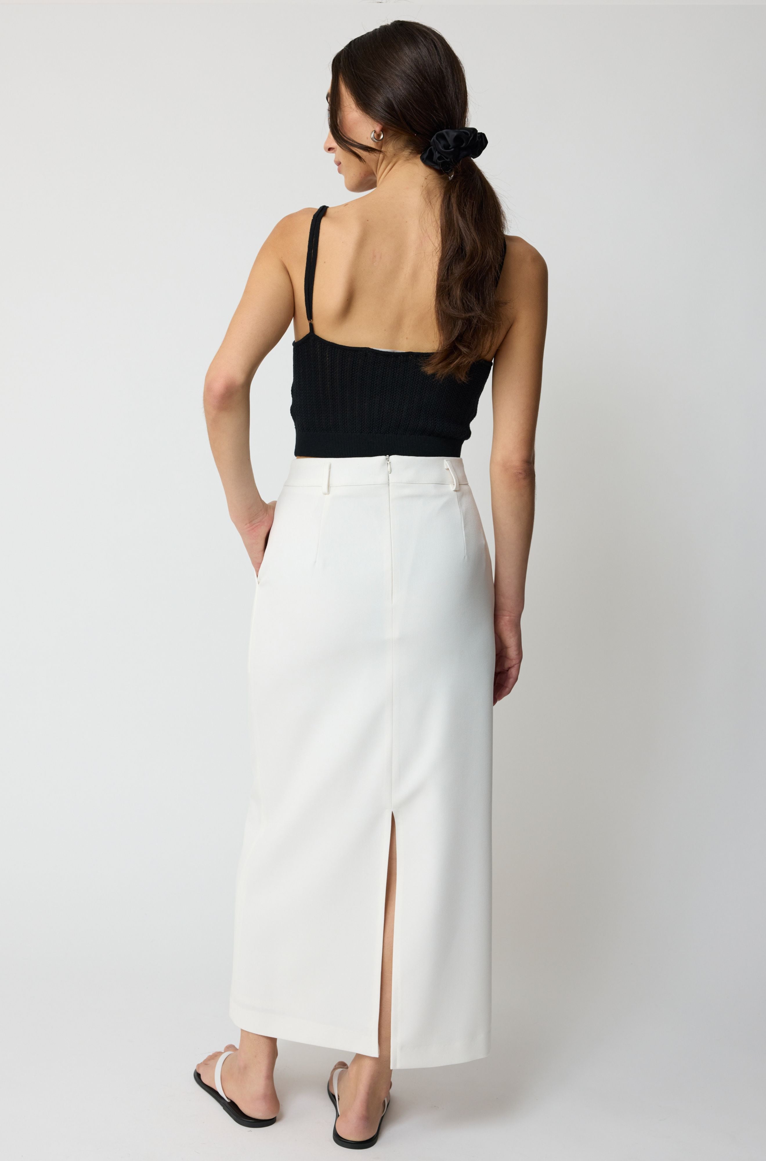 Woman wearing a black top and white skirt on a plain background