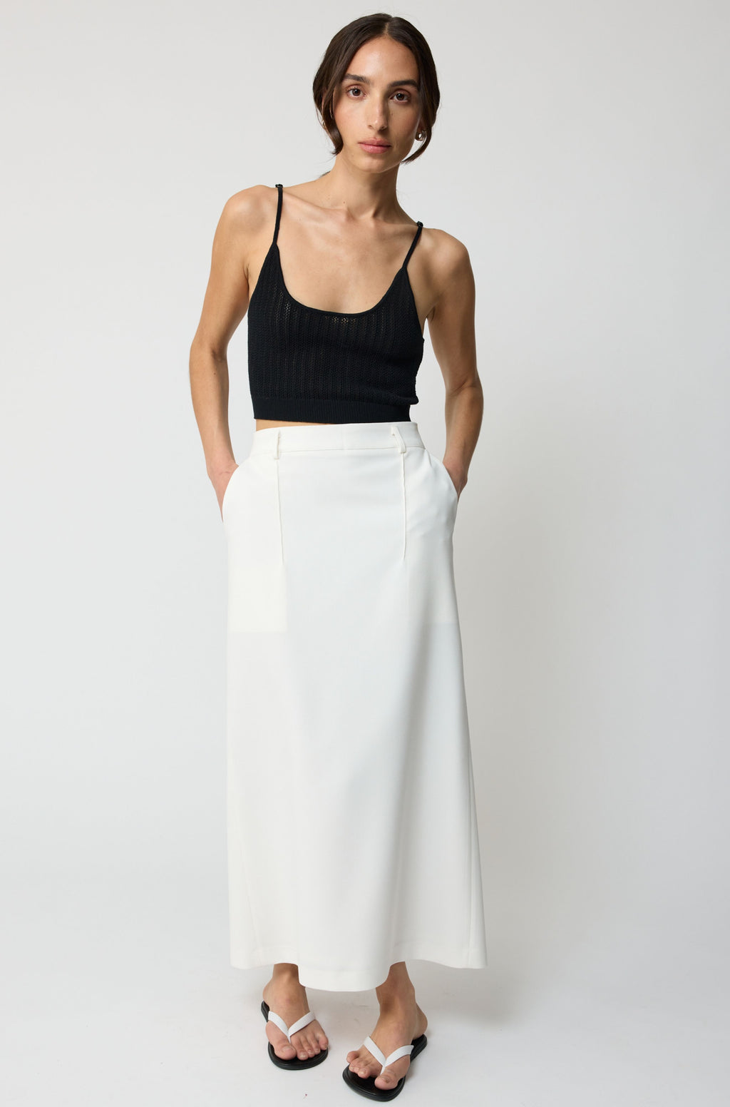 Woman wearing a black tank top and white skirt on a plain background