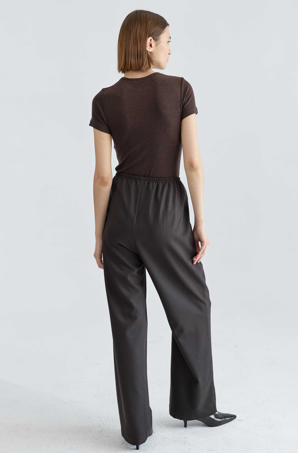 Woman wearing a brown top and dark brown pants on a light gray background