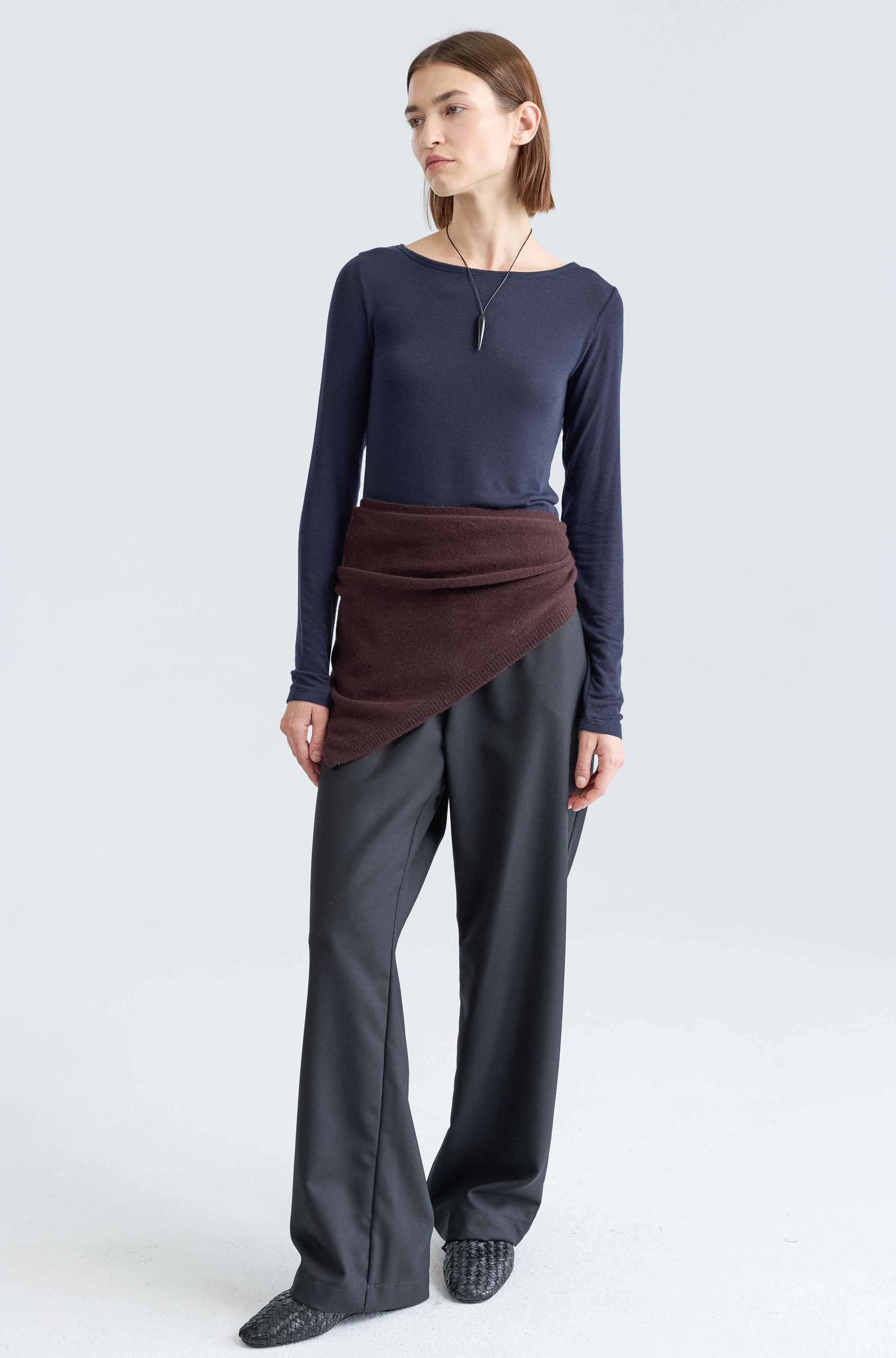 Woman wearing a navy long-sleeve top and gray pants on a white background