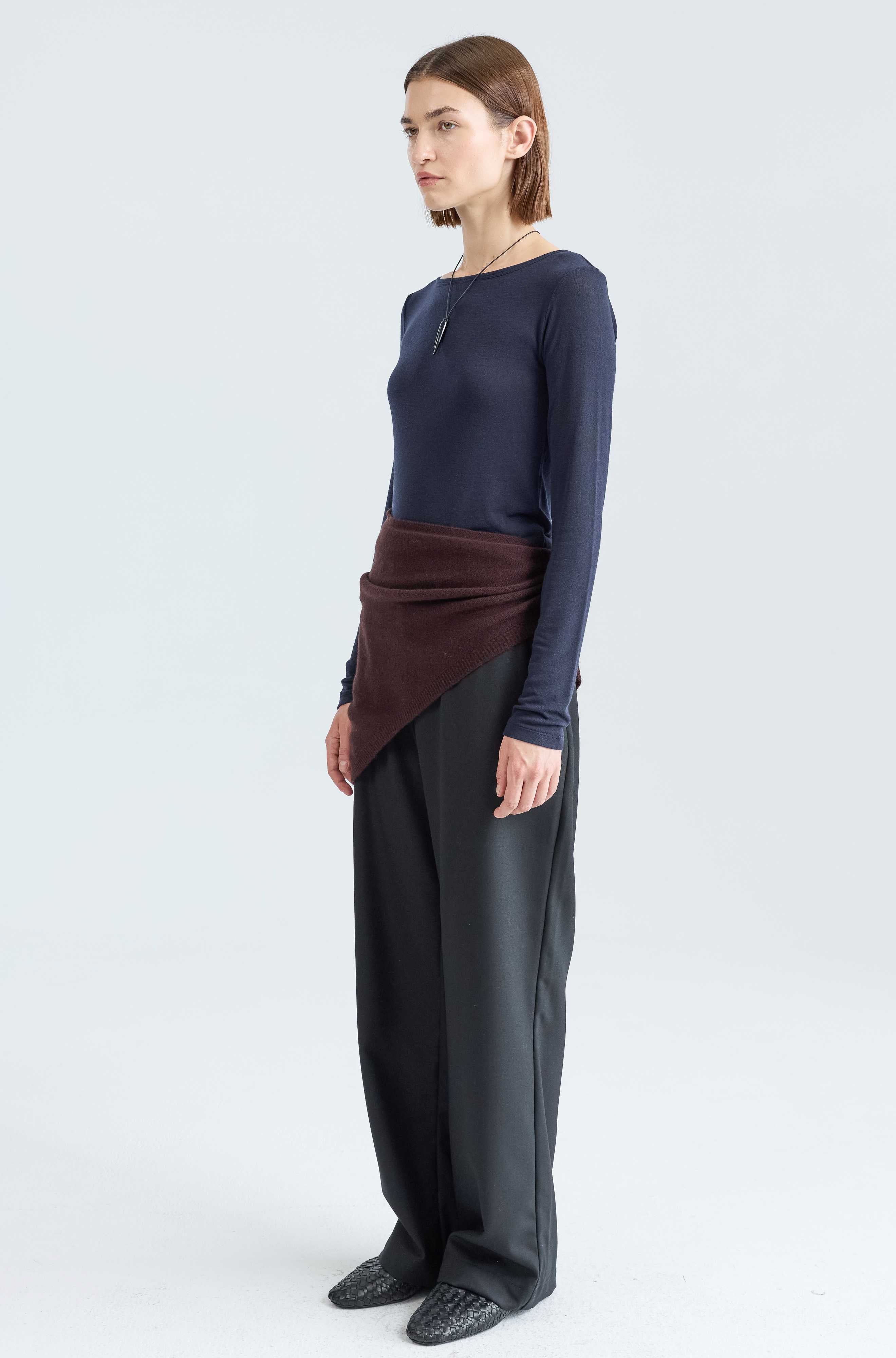 Person wearing a navy long-sleeve top and black pants with a brown accent on a white background