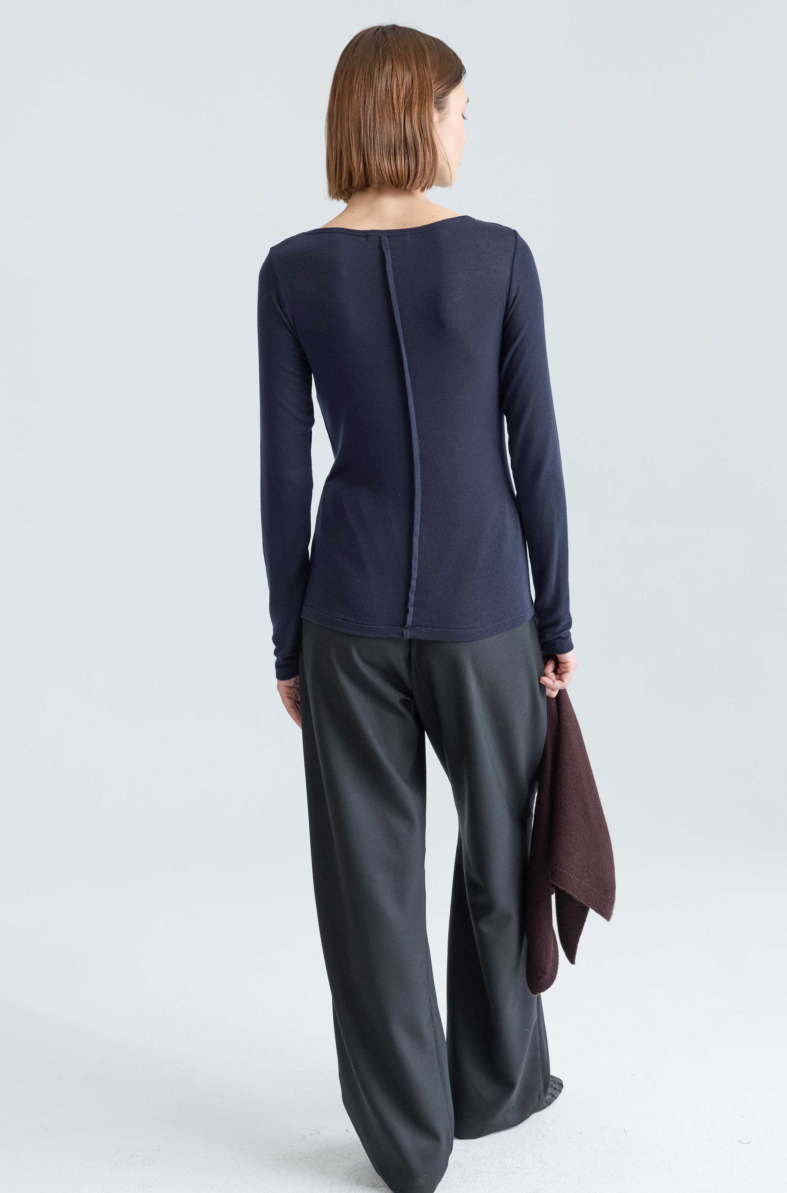 Woman wearing a navy long-sleeve top and dark gray pants on a white background