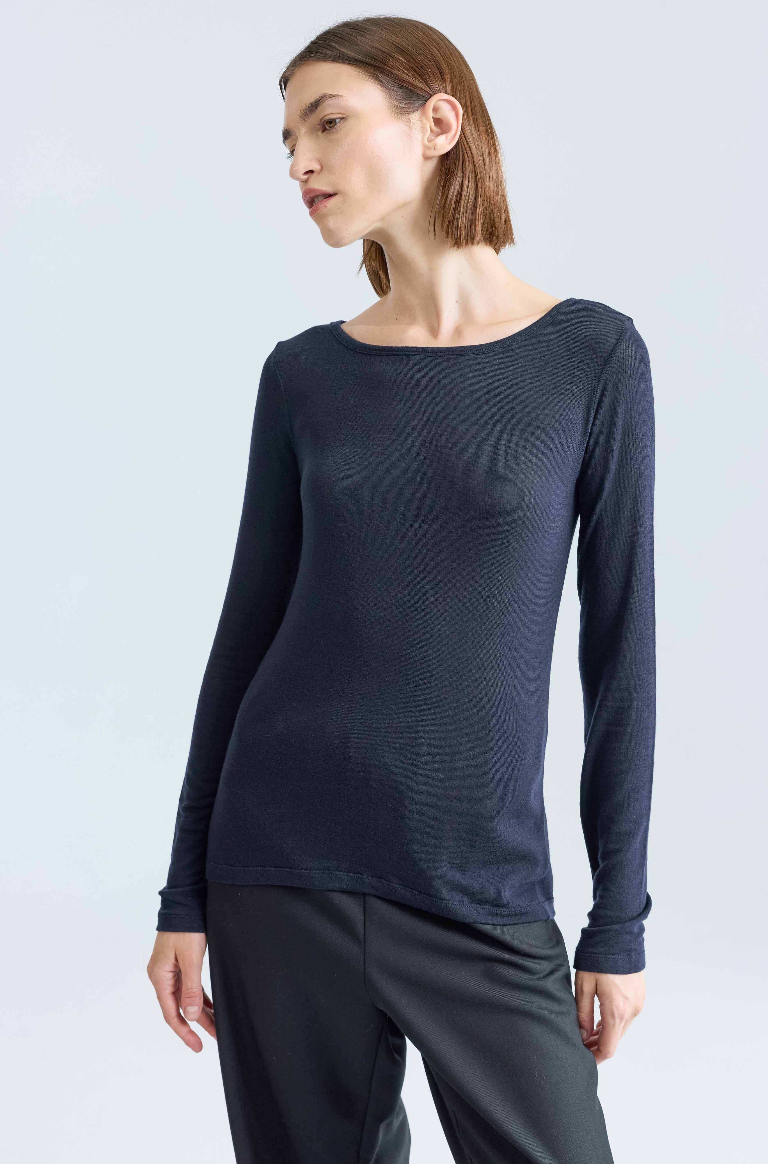 Woman wearing a navy long-sleeve top and gray pants on a light gray background