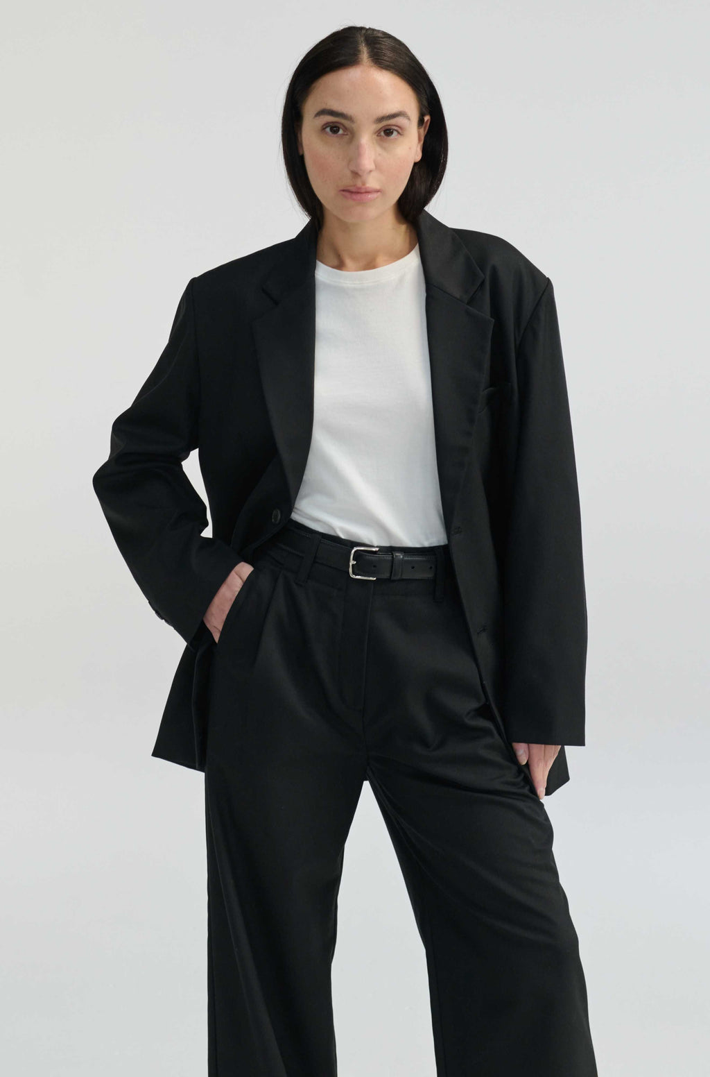 Person wearing a black blazer and black pants with a white shirt on a light gray background