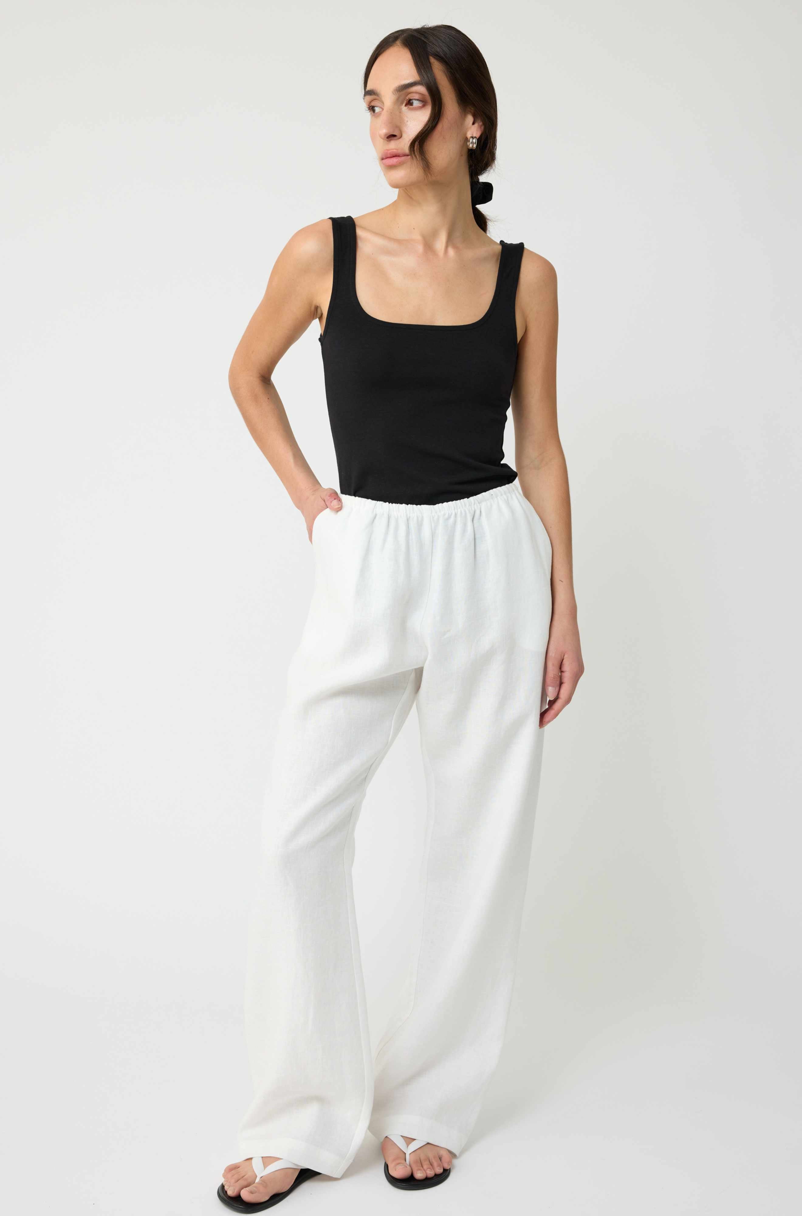 Woman wearing a black tank top and white pants on a white background