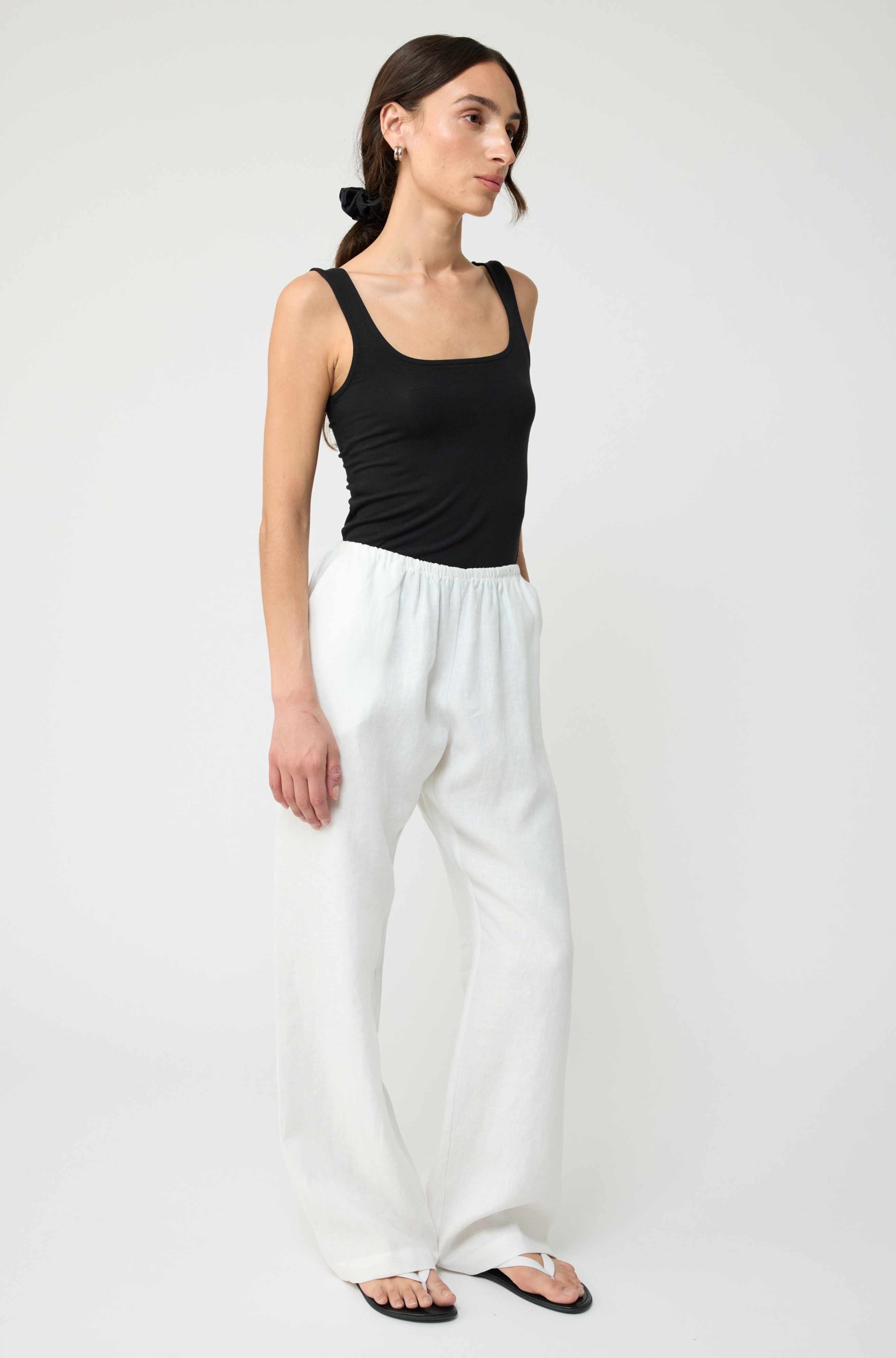 Woman wearing a black tank top and white pants on a white background