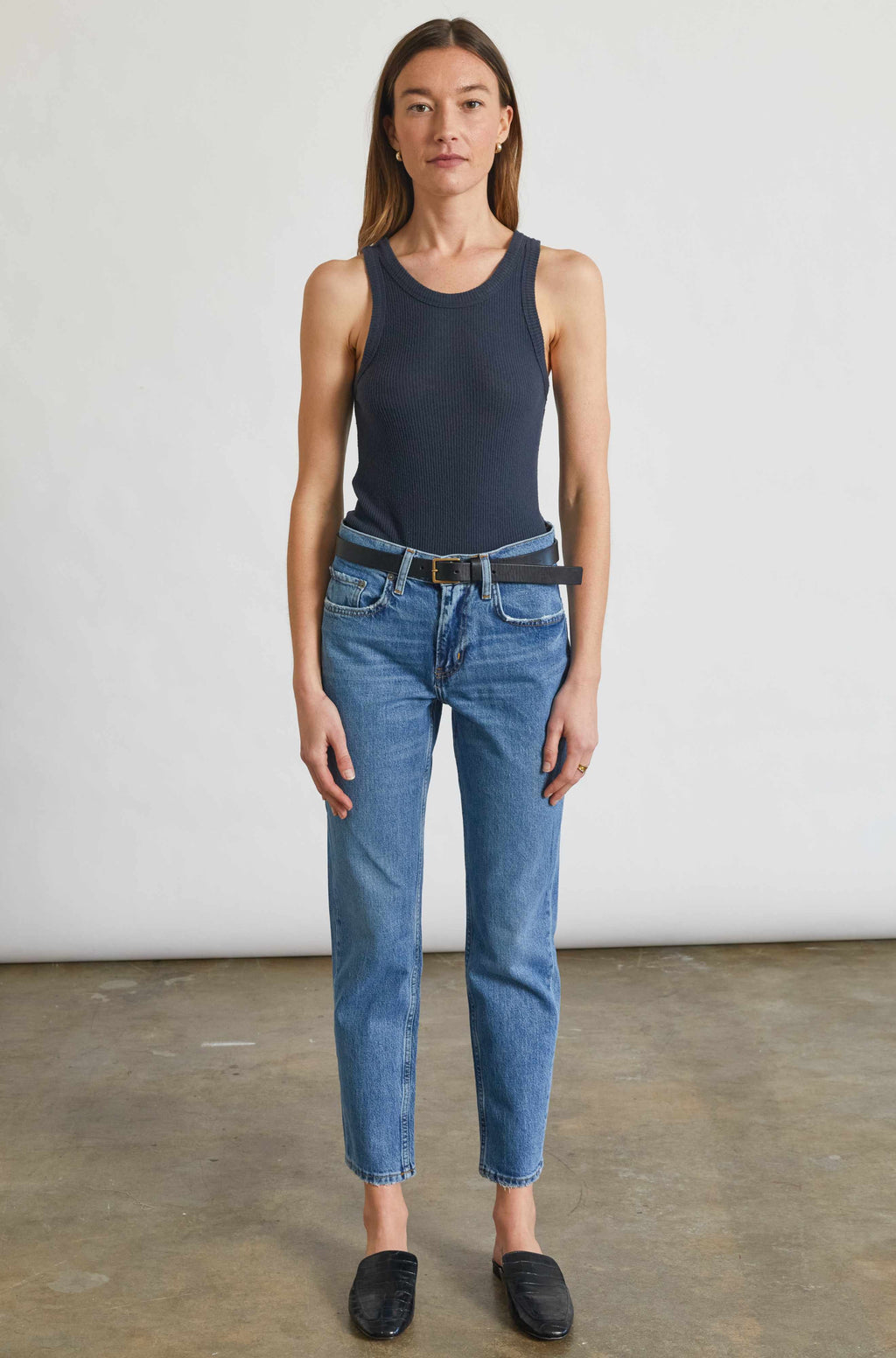 Woman wearing a navy tank top and blue jeans standing against a plain white background