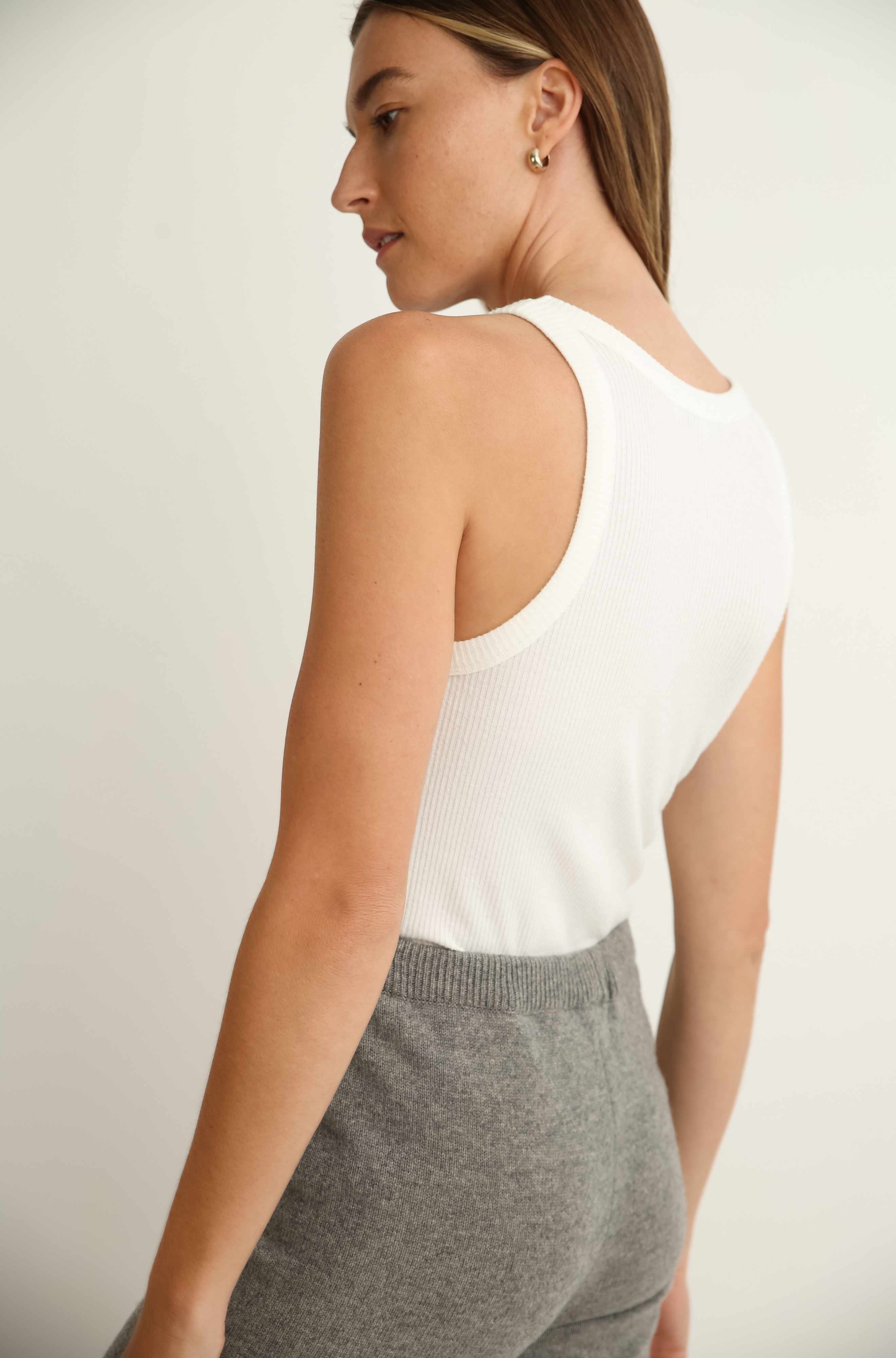 Woman wearing a white sleeveless top and gray pants against a plain background
