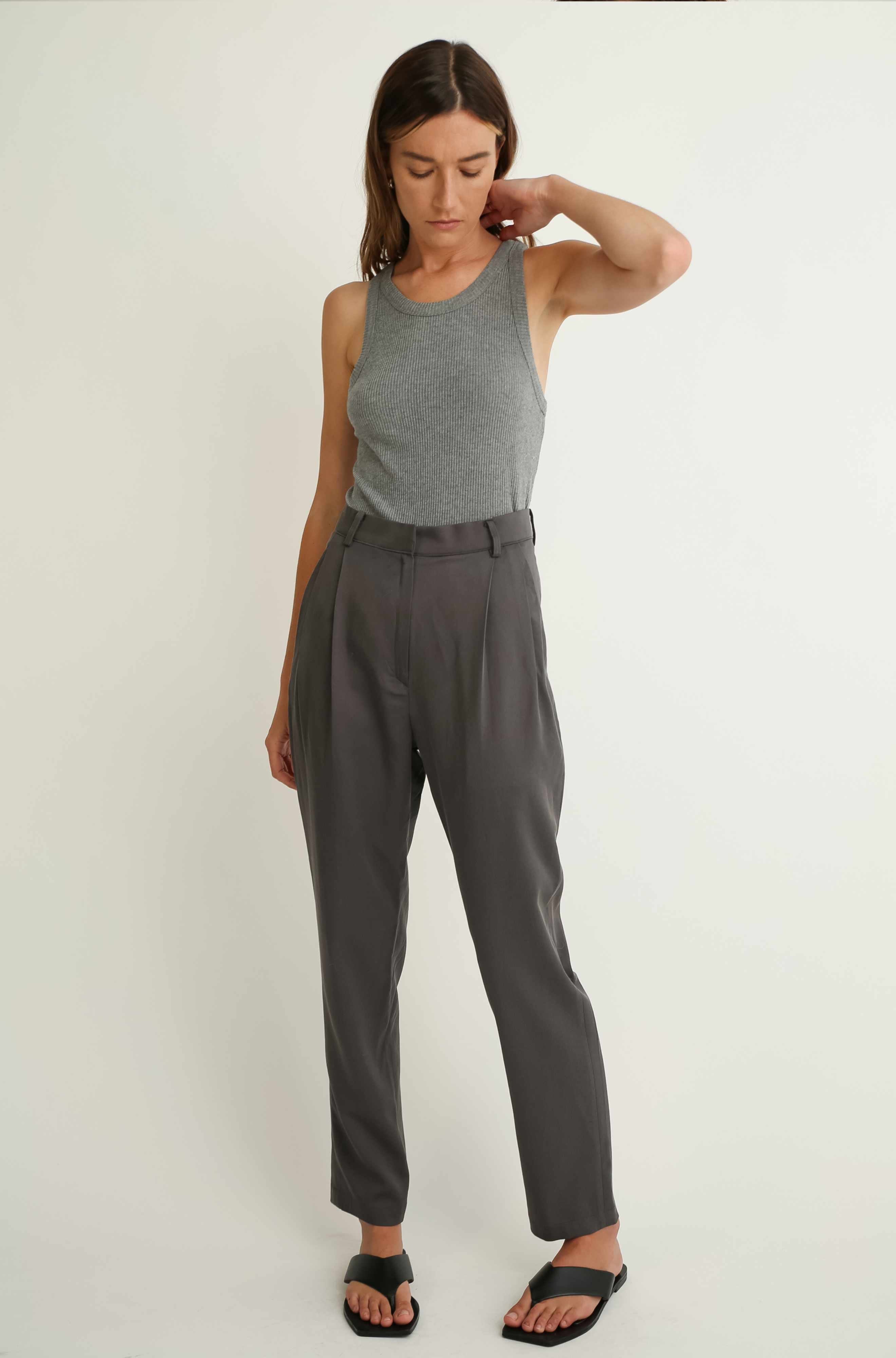 Woman wearing a gray sleeveless top and high-waisted pants on a white background