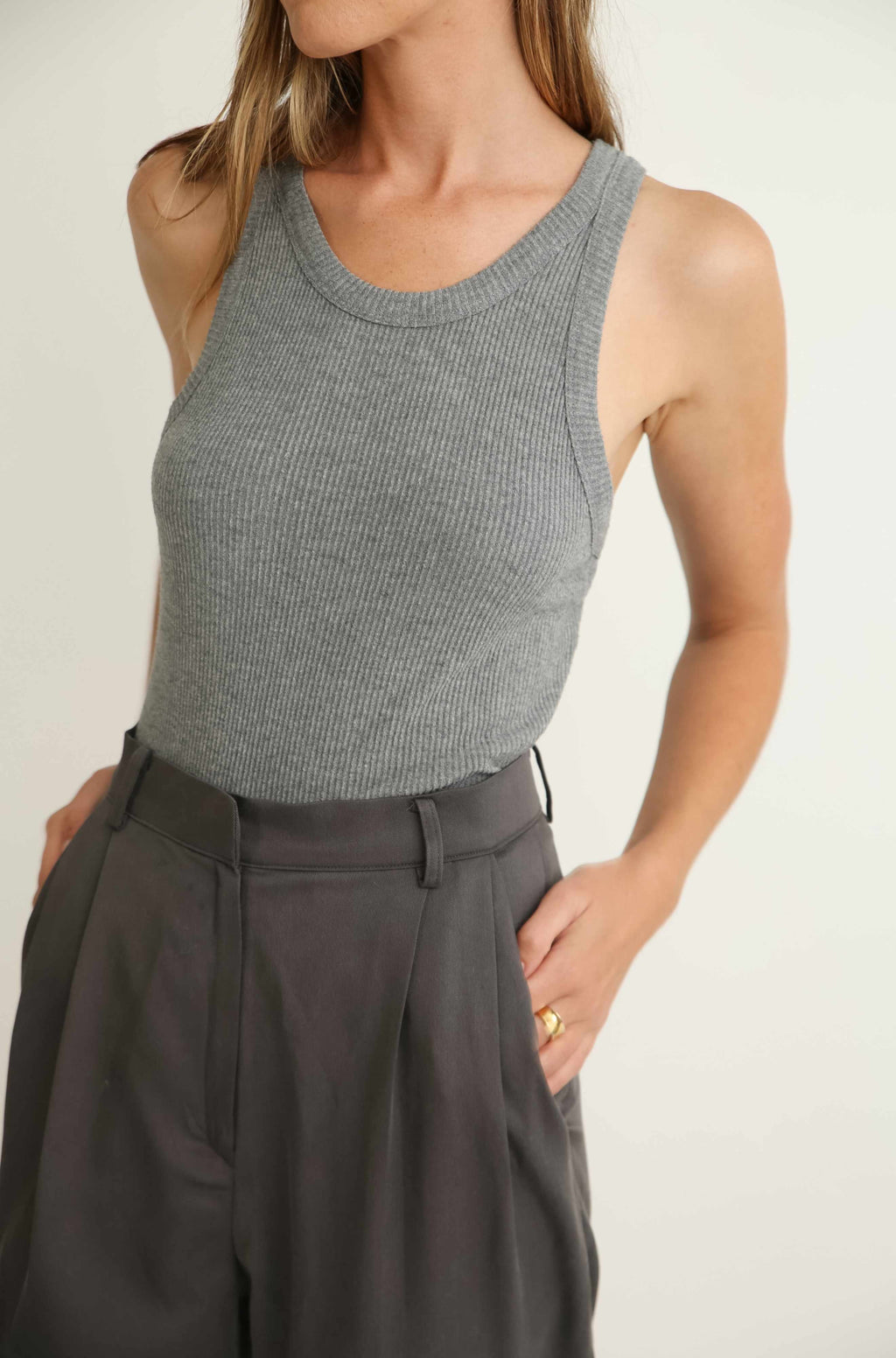 Person wearing a gray sleeveless top and dark pants on a plain background