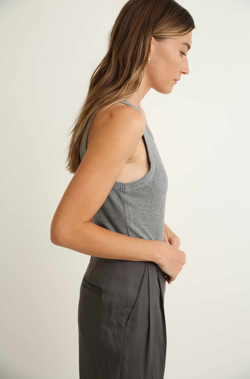 Woman wearing a gray sleeveless top and pants against a plain background