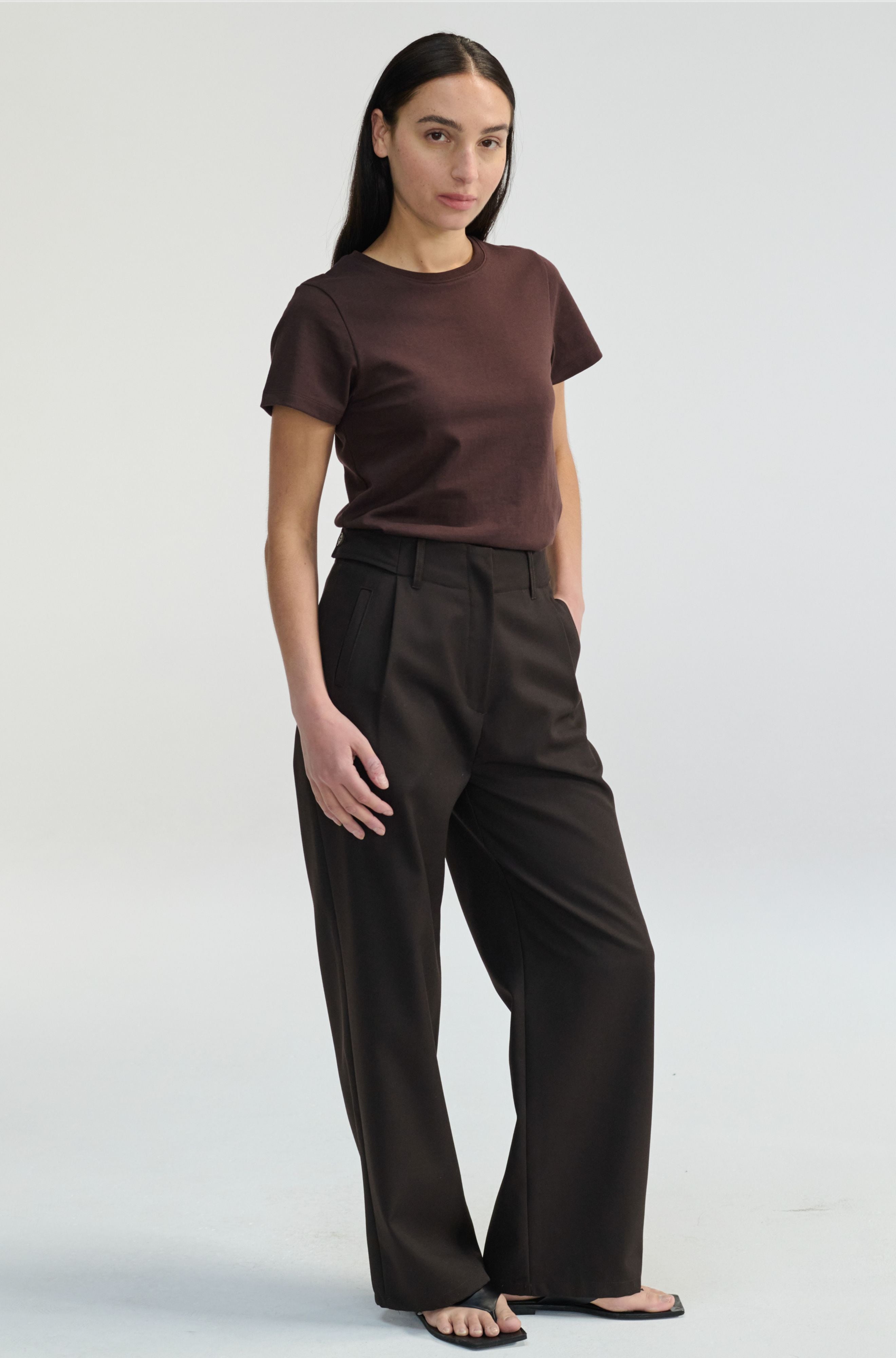 Woman wearing a brown t-shirt and dark brown pants on a white background