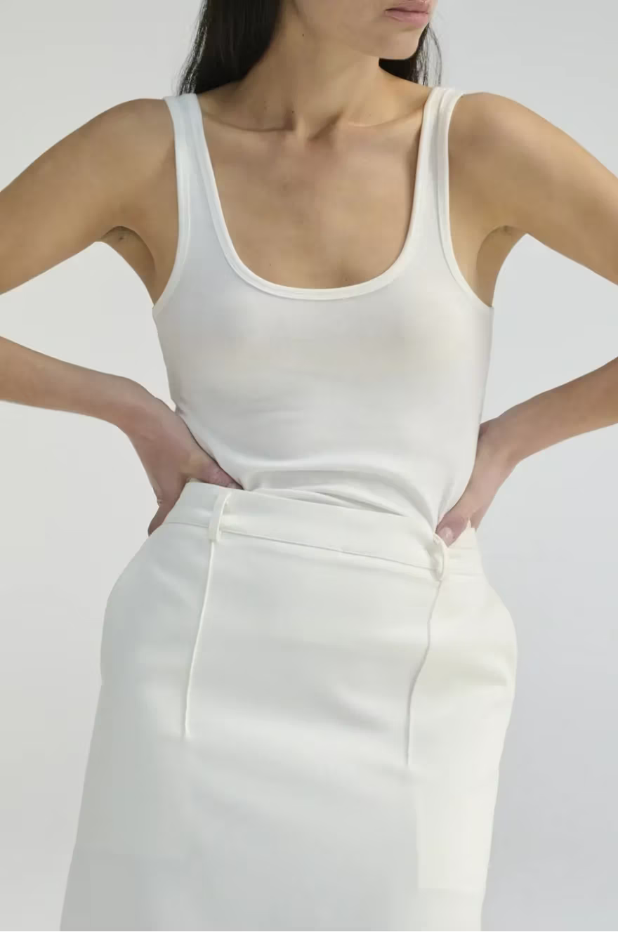 Woman wearing a white tank top and a white skirt against a plain background