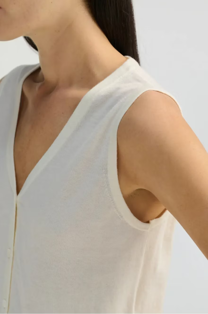 Close-up of a person wearing a white sleeveless top against a light background